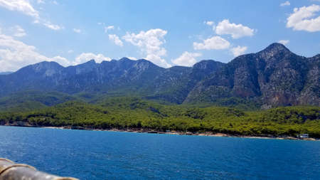 blue sea, coastline and mountains overgrown with forest under a blue sky with white cloudsの写真素材