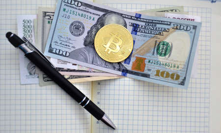gold coin bitcoin and dollars lie next to the pen on a background of papers in a cageの写真素材