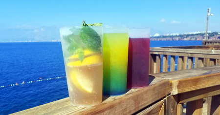 three multi-colored glasses with soft drinks against the background of the blue seaの写真素材