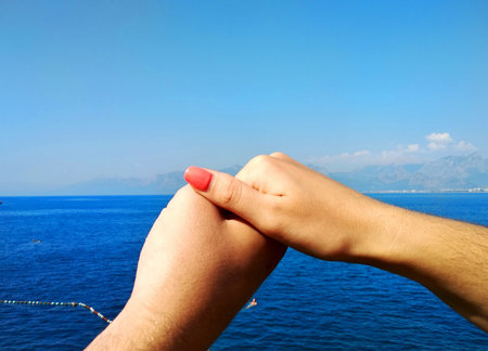 a man's hand holds a woman's hand on a background of blue sea and blue sky