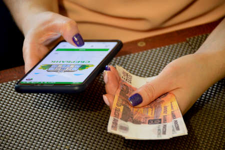 female hands hold a switched on smartphone and a bundle of bills of five thousand Russian rublesの写真素材