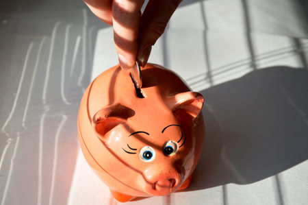 piggy bank in the form of a pig on a light background, a woman's hand puts a coin into the piggy...