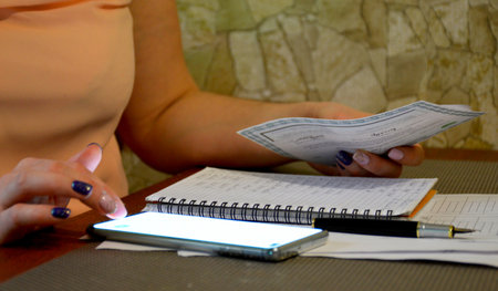 the table is filled with documents, next to female hands are holding papers and pressing something...