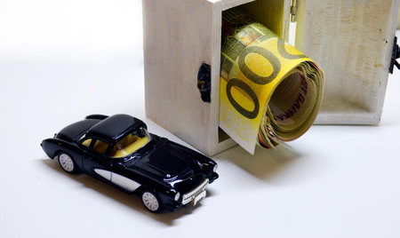 toy car and upside-down chest with paper money on light background