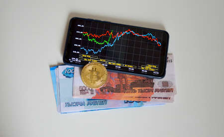 bitcoin coin, money and smartphone lie on a light background, on the smart phone screen stock chartの写真素材