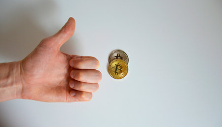 gold bitcoin coin and a man's hand on a light background, the thumb is raised up, shows a "like" signの写真素材