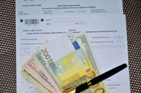 tax declaration form in Russian and paper banknotes of dollars and euros, next to it lies a black penの写真素材