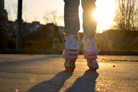 female legs shod in rollers against the backdrop of the setting sun, a woman stands on a flat surface and is ready to move, the sun seems to be shining through her legの写真素材