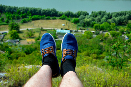 male legs shod in denim loafers on the edge of the cliff, in the background a blurred background of...