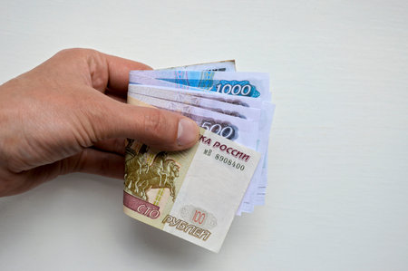 Russian paper money of various denominations stacked in a man's hand on a white background