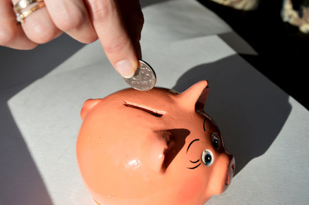 close-up of a female hand that puts a Russian coin into a piggy bank in the form of a pig on a white...