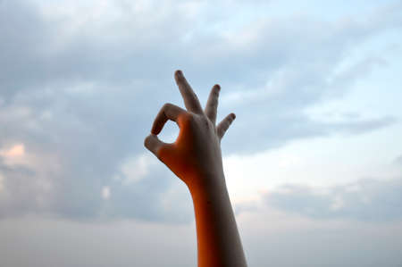 the hand of a young girl folded on a background of the sky during sunset symbol okayの写真素材