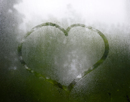 The heart is drawn on glass. The glass is fogged up and there are many drops on it
