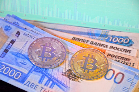 two coins, gold and silver bitcoins, lie on Russian banknotes of various denominations against the...
