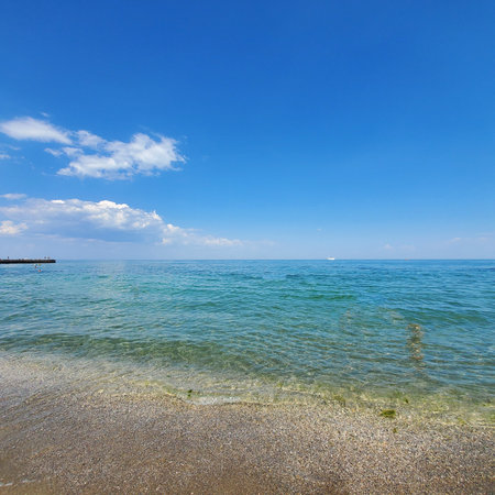 Sea pebble beach, and above the blue sky with white clouds. Beach and sea with turquoise water....