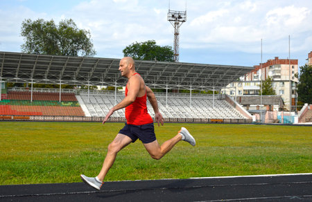 young muscular athlete runs on a black rubber treadmill in the stadium. outdoor training. active...