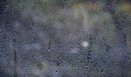 Raindrops on window glass surface with trees and nature blurred background