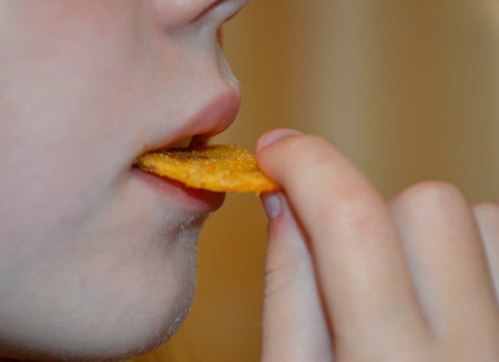 A young girl eats potato chips, a close-up of a woman's mouth bites the chips, copy space. unhealthy diet, fats and carcinogens in foodの写真素材