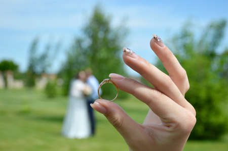 a gold engagement ring with a stone in a womans hand in the background a blurred silhouette of a couple in love kissing during a wedding photo shootの写真素材