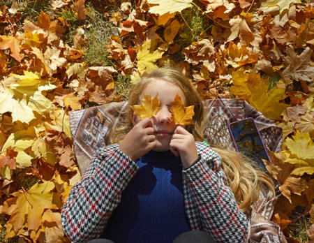 a beautiful girl lies on the fallen leaves in the autumn park and looks up. covered her eyes with...