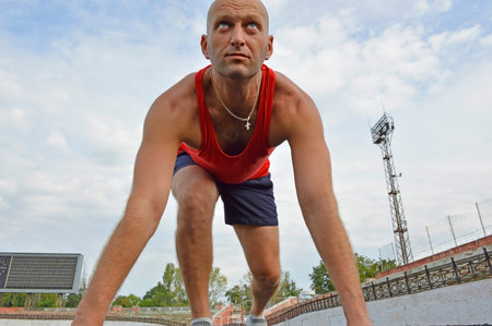 bald male athlete doing push-ups on the rubber floor at the stadium. outdoor training. active...