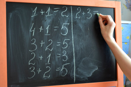 learning math at home on a small blackboard. teacher's hand with chalk writes examples on the blackboard. primary education, preparation for schoolの写真素材