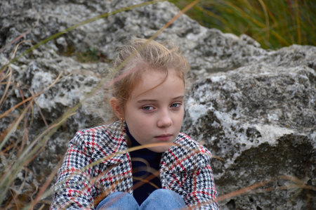 beautiful girl in a plaid coat on a walk in the autumn park posing near a large stone. the child smiles and looks a little to the side. active lifestyle and outdoor activities. attractive peopleの写真素材