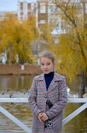 cute beautiful girl in a stylish plaid coat on a walk in the autumn park. teenager smiles and shyly looks into the camera. active lifestyle and outdoor activitiesの写真素材