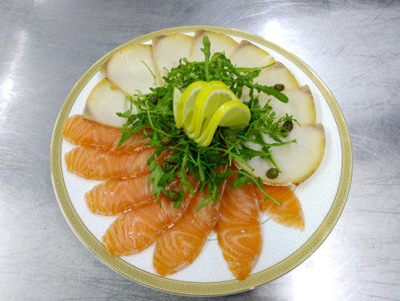 a large plate of sliced salmon and pieces of butterfish. Garnished with herbs and lemon slices. cold appetizer from valuable tasty species of marine fishの写真素材