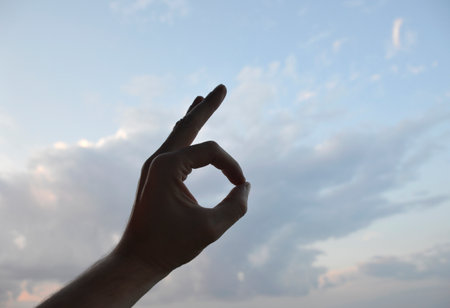 silhouette of a hand, against the background of the sky at sunset, shows a symbol with fingers. message or gestures. silence and beauty in natureの写真素材