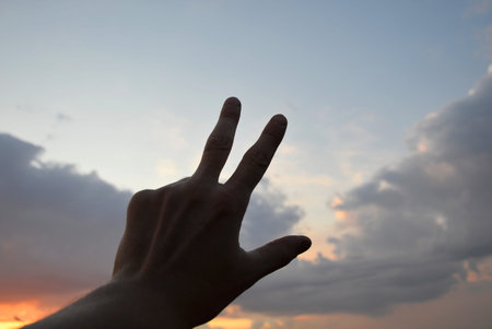 silhouette of a hand, against the background of the sky at sunset, shows a symbol with fingers. message or gestures. silence and beauty in natureの写真素材