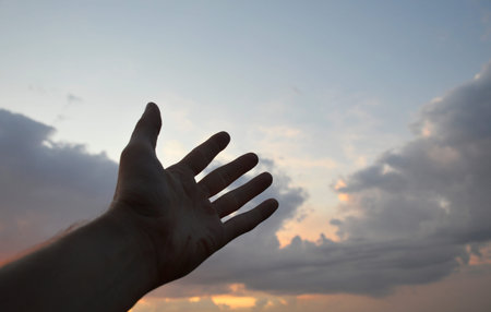 silhouette of a hand, against the background of the sky at sunset, shows a symbol with fingers....