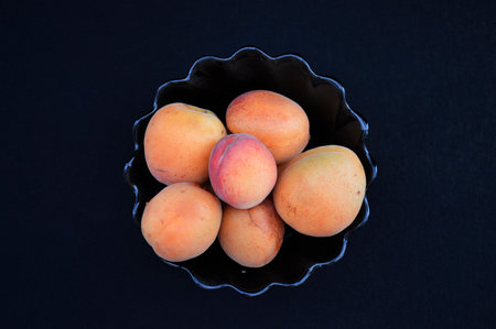 fresh, ripe apricots in a glass bowl on a black background. tasty, wholesome, proper and healthy food. fruits rich in vitamins and antioxidants for dessert for children and adultsの写真素材