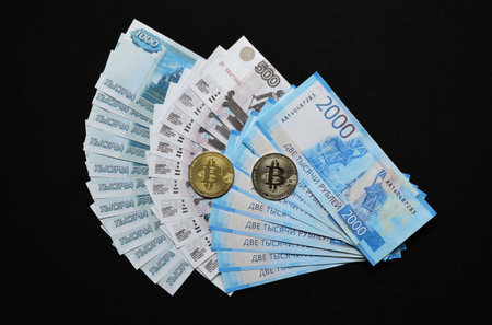 two bitcoins and Russian rubles spread out like a fan on a black background. the concept of abandoning paper money and switching to cashless payments, virtual currency and e-commerceの写真素材