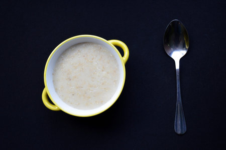 bowl with oatmeal cooked in milk and a spoon on a black background. delicious and healthy breakfast for children and adults. proper and dietary nutritionの写真素材