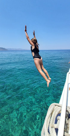 a girl jumps from the side of a yacht into turquoise sea water. boat trips on the open sea. fun and relaxation during vacation or vacation. travel destinationの写真素材