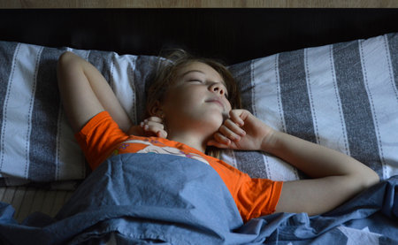 beautiful girl in bed stretches after sleep. the child's eyes are closed. last minutes of sleep before waking upの写真素材