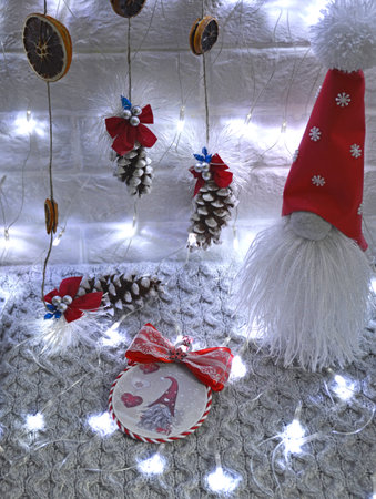 Christmas and New Year decoration with gnomes, pine trees and garlands. a large gnome in a red cap and with a white, fluffy beard among the pine cones in the light of a white garlandの写真素材