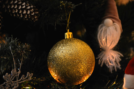 A large yellow, shiny ball hangs on a Christmas tree branch surrounded by other toys. celebrating Christmas and New Year. home and office decoration. festive and cheerful moodの写真素材