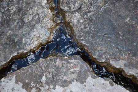 A deep crack in the road surface is filled with water after rain. The old concrete surface on the road was cracked due to weather conditions. dangerous driving on the roadの写真素材