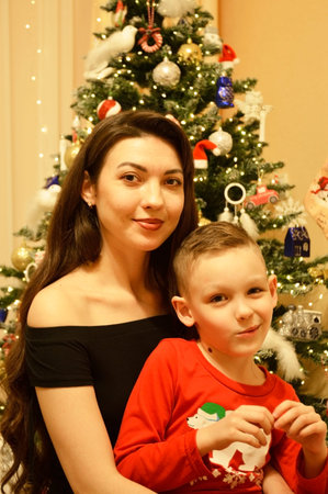A woman and a boy sitting on the floor in front of a decorated Christmas tree. Garlands, ornaments, and baubles glitter on the tree. The comfort and joy of a family holidayの写真素材