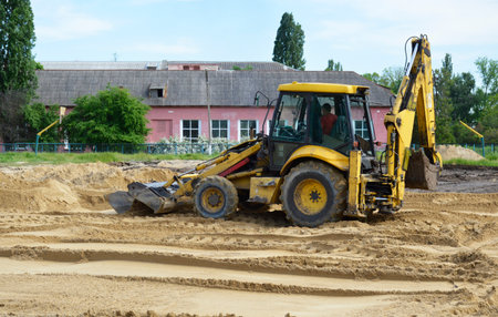 a yellow tractor with a blade and a bucket levels the sand at a construction site. construction machinery doing hard workの写真素材