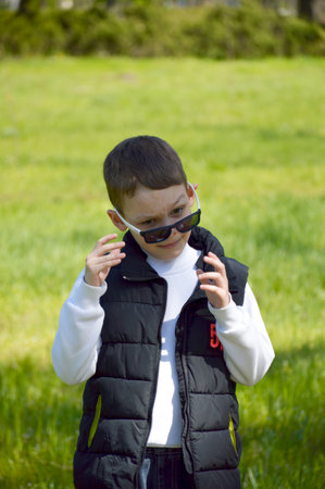 A boy standing against the backdrop of a green meadow on a sunny day. The child smiles slightly and looks away, creating a sense of naturalness and lightnessの写真素材