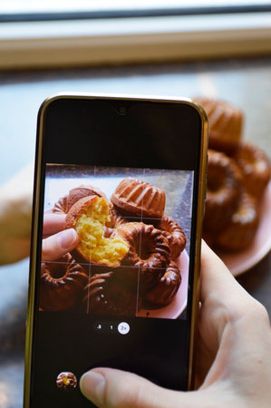 Women's hands holding a smartphone and photographing cupcakes. Freshly baked pastries for a food blog.の写真素材