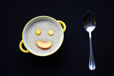 Oatmeal with ripe peach slices arranged in a smiley face. Delicious and healthy food for children and adults. Vitamins from fresh fruit and fiber in the porridge. Diet food.の写真素材