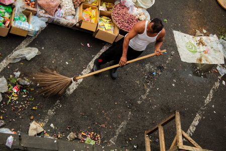 Semarang, Indonesia - February 5, 2018 : A man in a t-shirt holds a broomstick to clean up trash in...
