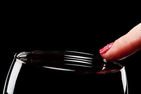 woman holds finger on a glass of wine on a black backgroundの写真素材