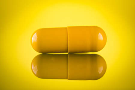one yellow pill capsule on glass backgroundの写真素材