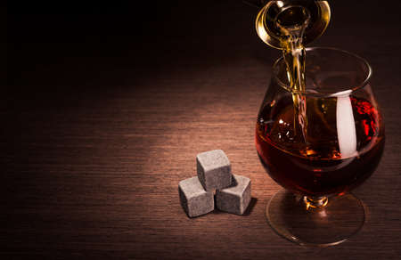 Pouring whiskey beverage in glass with stoneの写真素材