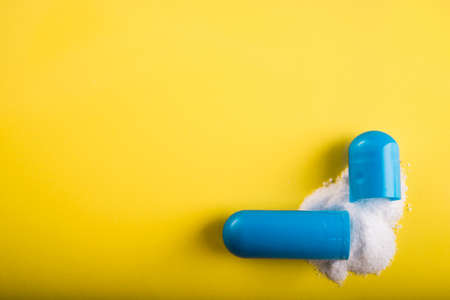 Open blue capsule pill with white powder drug on yellow backgroundの写真素材
